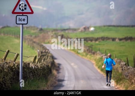 Shibden Valley, Halifax, West Yorkshire, Regno Unito. 16th aprile 2022. Meteo Regno Unito. Halifax, West Yorkshire in uno dei giorni più caldi dell'anno finora un corridore passa un segnale di avvertimento di ghiaccio su Corporal Lane nella valle di Shibden vicino Halifax. Credit: Windmill Images/Alamy Live News Foto Stock