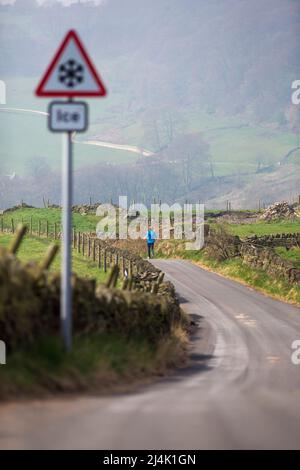 Shibden Valley, Halifax, West Yorkshire, Regno Unito. 16th aprile 2022. Meteo Regno Unito. Halifax, West Yorkshire in uno dei giorni più caldi dell'anno finora un corridore passa un segnale di avvertimento di ghiaccio su Corporal Lane nella valle di Shibden vicino Halifax. Credit: Windmill Images/Alamy Live News Foto Stock