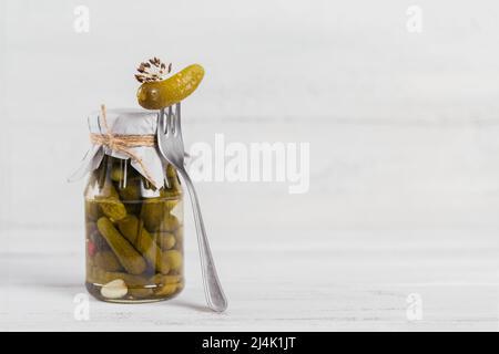 Cetrioli, cetrioli sottaceto su forchetta, verdure marinate in un vaso di vetro su sfondo bianco di legno Foto Stock