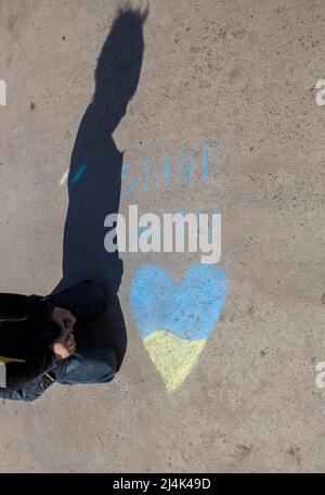 L'ombra contrastante di un bambino vicino al supporto dell'iscrizione con l'Ucraina e un cuore giallo-blu disegnato con pastelli sul marciapiede. I bambini vogliono la pace. DRA Foto Stock