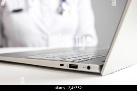 Medico con stetoscopio seduto alla scrivania con computer portatile. Donna in camice da laboratorio che dà la consultazione in linea al paziente. Concetto di assistenza sanitaria e telemedicina. Uso delle comunicazioni elettroniche per il trattamento. Foto Foto Stock