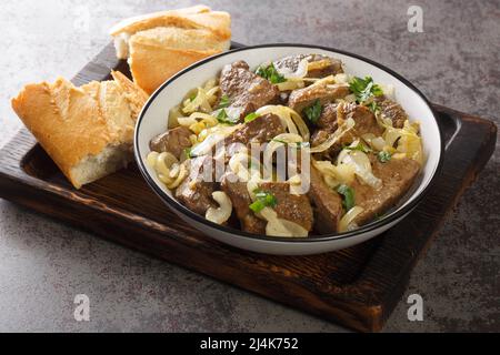 Cucina fatta in casa fegato di manzo fritto con cipolle ed erbe primo piano in un piatto e pane su un vassoio di legno sul tavolo. Orizzontale Foto Stock