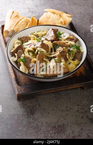 Primo piano fegato di manzo fritto con cipolle servito in un piatto su un vassoio di legno verticale Foto Stock