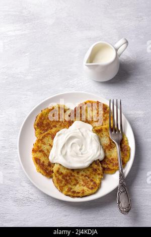 Frittelle tradizionali con crema acida su sfondo grigio chiaro testurizzato, vista dall'alto Foto Stock