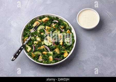 Insalata Kale con patate al forno, cetrioli, cipolle rosse e salsa di yogurt senape su sfondo grigio, vista dall'alto Foto Stock