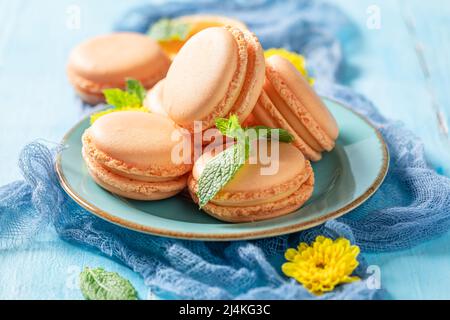 Gustosi e freschi macaron di frutta passione con fiori su tavola blu. Amaretti d'arancia a base di frutti della passione. Foto Stock