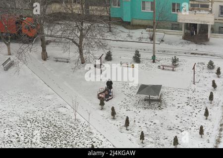 Scena invernale sul cortile da una vista a volo d'uccello. Una donna non identificata gioca sul parco giochi con i bambini durante una nevicata Foto Stock