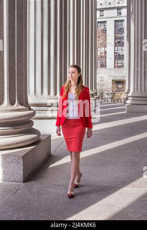 Vestendo un blazer rosso ed una gonna rossa chiara, una ragazza giovane adolescente sta camminando fuori di un edificio dell'ufficio. Foto Stock