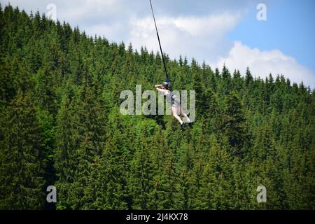 La ragazza saltò dal bungee saltando, si appende su una corda stretta ad un'altitudine elevata. Su uno sfondo sfocato di una montagna Foto Stock