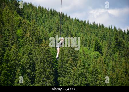 La ragazza saltò dal bungee saltando, si appende su una corda stretta ad un'altitudine elevata. Su uno sfondo sfocato di una montagna Foto Stock