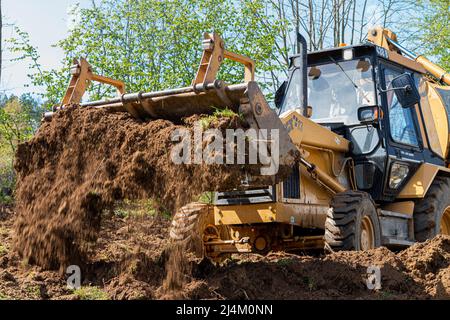 Spianando e livellando un terreno privato. Escavatore giallo che guida la terra in una benna larga Foto Stock