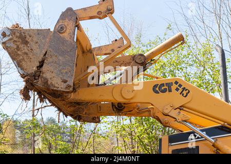 Spianando e livellando un terreno privato. Escavatore giallo che guida la terra in una benna larga Foto Stock