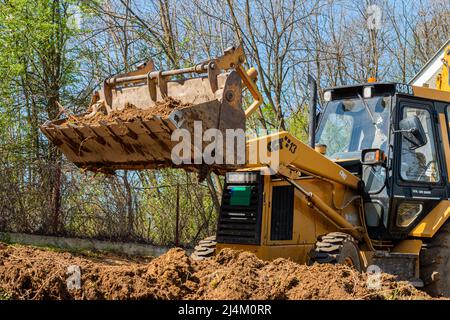 Spianando e livellando un terreno privato. Escavatore giallo che guida la terra in una benna larga Foto Stock
