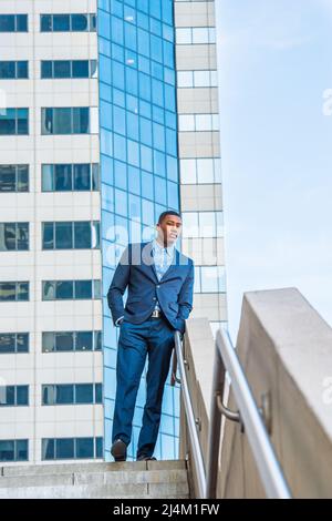 Un giovane bel uomo d'affari nero è in piedi fuori di un business building, rilassante e pensante. Foto Stock