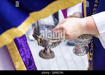 Un ragazzo altare o un'accolita in una processione della settimana Santa che riempe uno dei censori di incenso. La fotografia a fuoco selettivo con messa a fuoco ai margini del Foto Stock