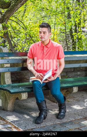 Vestendo in una polo rossa, pantaloni verdi e lunghi stivali in pelle, un giovane ragazzo bello è seduto su una lunga sedia la mattina di una stagione primaverile, Foto Stock