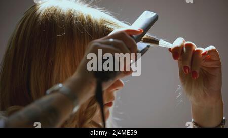 La ragazza avvolge i ricci su un ferro arricciante. ARTE. La ragazza ha capelli biondi che arriccia. Capelli arricciati Foto Stock