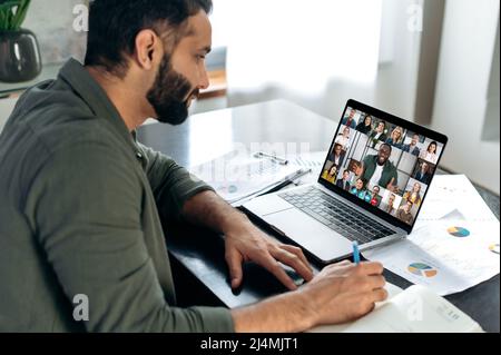 Un uomo indiano di successo che utilizza un laptop, conduce incontri virtuali con i partner aziendali durante una videochiamata. Gruppo di diversi uomini d'affari multirazziali sullo schermo di un portatile che parlano da videoconferenza Foto Stock