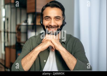 Ritratto di bel positivo indiano o arabo uomo indossando cuffie, esperto, consulente o mentore, guarda direttamente la fotocamera, sorride amichevole, conduce la consultazione. Concetto di servizio di supporto, hotline Foto Stock