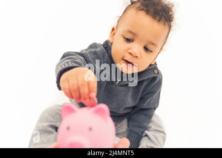 Bambino ragazzo giovane usando la banca rosa del piggy mettendo le monete là. Concetto di risparmio e futuro. Studio girato su sfondo bianco. Foto di alta qualità Foto Stock