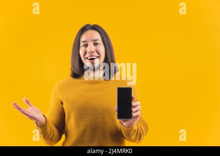 Il giovane eccitato che mostra schermo nero di smartphone alla fotocamera e mantenere un'altra mano aperta annunci e promozione concetto di copia spazio giallo sfondo studio girato isolato . Foto di alta qualità Foto Stock