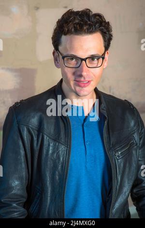 Ritratto di giovane Scholar. Giovane uomo che indossa occhiali neri, giacca in pelle nera, in piedi accanto alla parete, guardando avanti. Foto Stock