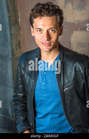 Vestirsi in una giacca di pelle nera, una camicia blu, un ragazzo giovane e bello ti sta guardando con fascino. Foto Stock