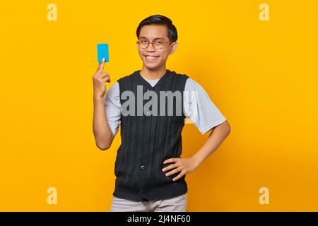 Ritratto di attraente uomo asiatico ridendo e tenendo carta di credito su sfondo giallo Foto Stock