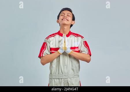 Uomo meccanico che indossa uniforme pregando con le mani insieme chiedendo perdono sorridendo con fiducia Foto Stock