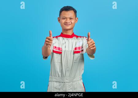 Ritratto di giovane meccanico asiatico sorridente che mostra il pollice su gesto isolato su sfondo blu Foto Stock