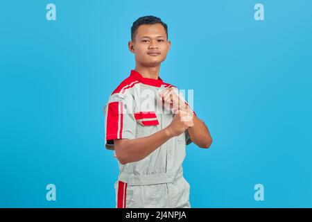 Ritratto di giovane meccanico asiatico arrabbiato che mostra il gesto del pugile su sfondo blu Foto Stock