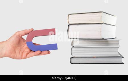 Donna mano che tiene magnete vicino a libri stack. Attrarre, ottenere conoscenza, saggezza dalla lettura. Concetto di istruzione e studio. Foto di alta qualità Foto Stock