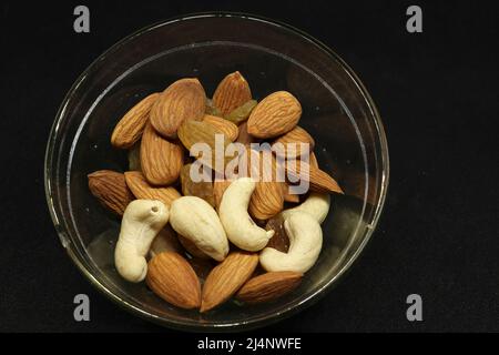 La frutta secca sana, la mandorla, le seghe e l'uva sono in una tazza. Su sfondo nero Foto Stock