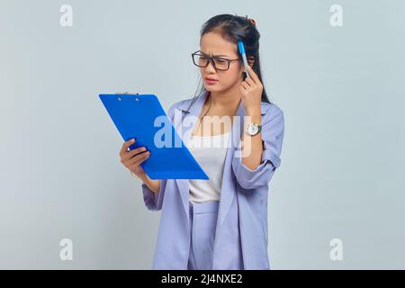 Ritratto della giovane donna asiatica d'affari graffiare testa con penna, pensare di idee e tenere appunti isolato su sfondo viola Foto Stock