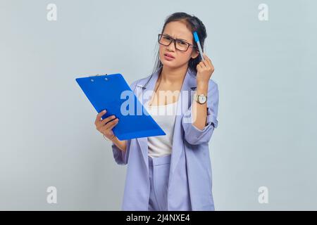 Ritratto della giovane donna asiatica d'affari graffiare testa con penna, pensare di idee e tenere appunti isolato su sfondo viola Foto Stock