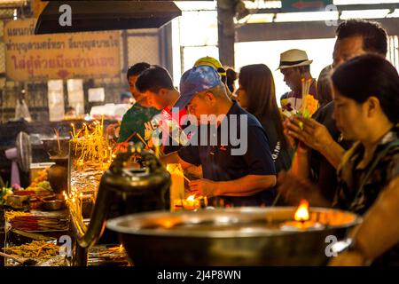 Una linea di gente illumina l'incenso ad un tempio buddista locale di Bangkok. Foto Stock