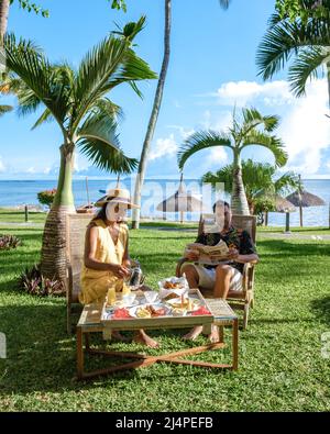 Colazione in una spiaggia con palme e una piscina a Mauritius, un ambiente tropicale con colazione. Coppia uomo e donna che fa colazione in giardino tropicale Foto Stock