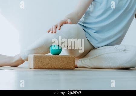 Primo piano di una persona che fa il rilascio miofasciale con la sfera di massaggio sulla gamba interna inferiore. Concetto: Salute del ginocchio, pratiche di cura di sé a casa Foto Stock