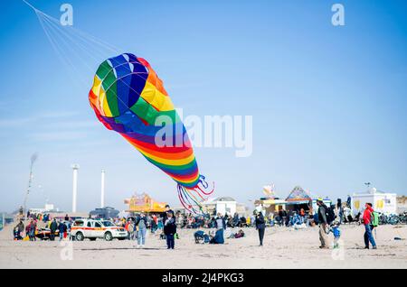 Norderney, Germania. 17th Apr 2022. Un aquilone colorato vola nel vento contro un cielo blu su Weststrand, mentre sullo sfondo numerosi turisti guardano la tradizionale 'Eiertrullern'. In questa consuetudine frisone orientale, le uova di Pasqua sode vengono arrotolate da una collina in una gara. Credit: Hauke-Christian Dittrich/dpa/Alamy Live News Foto Stock