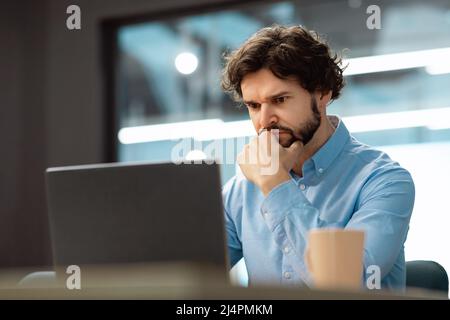 Uomo d'affari concentrato che utilizza un computer portatile seduto alla scrivania Foto Stock