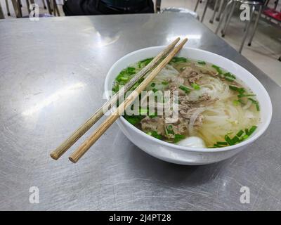 Pho Bo, una zuppa di noodle di manzo e riso servita in un ristorante con bacchette, Vietnam. Foto Stock