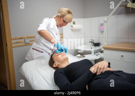 Medico Beutician strofinando il viso del paziente con tamponi di cotone. Ritratto di donna sulla pulizia del viso procedura da cosmetologo donna in clinica di bellezza. Bellezza Foto Stock