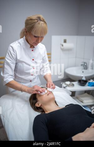 Medico Beutician strofinando il viso del paziente con tamponi di cotone. Ritratto di donna sulla pulizia del viso procedura da cosmetologo donna in clinica di bellezza. Bellezza Foto Stock