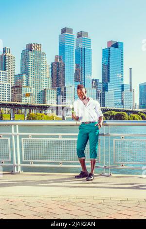 Ti manca. Indossando una camicia bianca, pantaloni verdi, scarpe in pelle, un giovane ragazzo nero con capelli mohawk si erge davanti agli edifici, tenendo rosa bianca Foto Stock