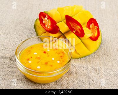 Marmellata di peperoncino mango in recipiente di vetro, mango a dadini e pepe tagliato in burlap Foto Stock