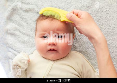 La mamma pettina un neonato con una speciale spazzola per capelli. Concetto di maternità. Igiene del bambino Foto Stock
