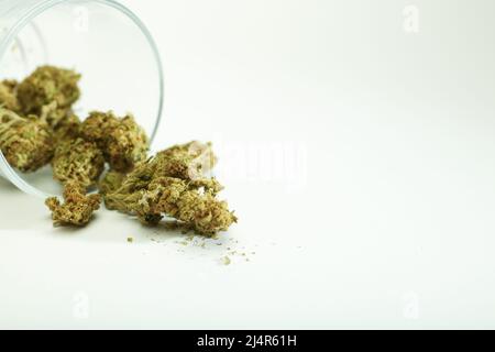 boccioli di marijuana che escono dal contenitore di vetro su sfondo bianco , spazio per il testo. Foto Stock