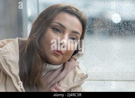 Una donna o un modello piuttosto giovane che attende sgombrosamente a una fermata dell'autobus in una giornata piovosa, Edimburgo, Scozia, Regno Unito Foto Stock