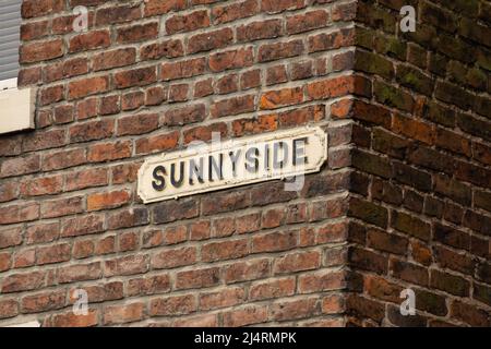 Vecchio cartello di strada con intemperie su muro di mattoni nella città inglese. Foto Stock