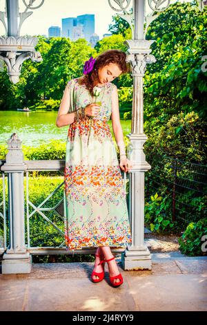 Lady Missing You at Park. Vestirsi in sleeveless, verde chiaro, vestito lungo, scarpe di sandali rosse, ragazza graziosa teenage che sta all'interno del padiglione, holdi mano Foto Stock